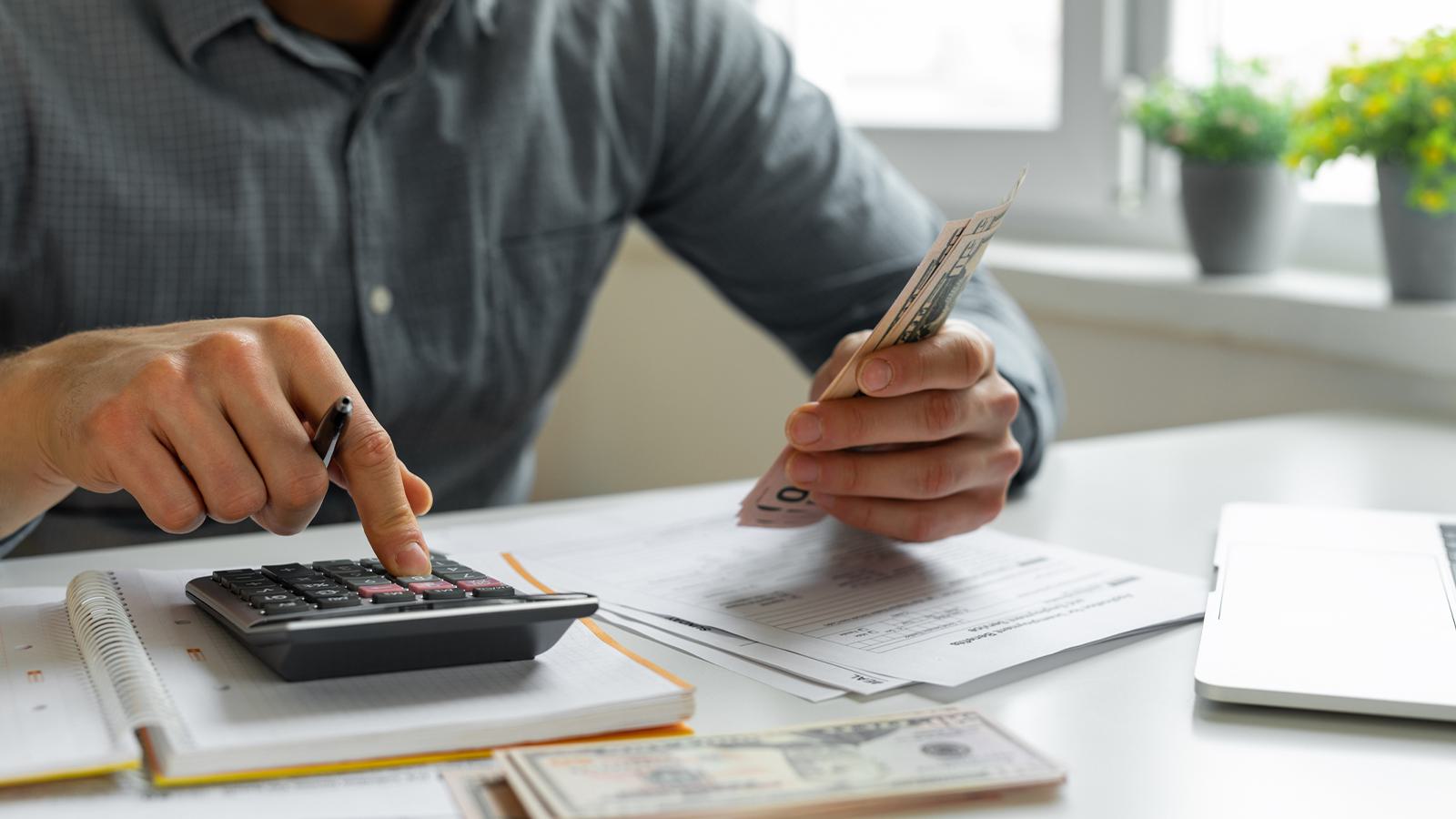 man holding money and typing on calculator